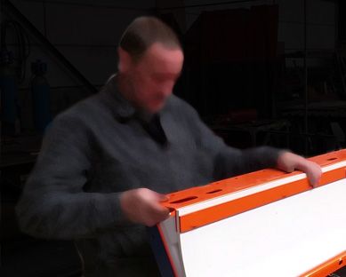 Ouvrier en atelier manipulant un panneau orange et blanc d'auge de convoyeur