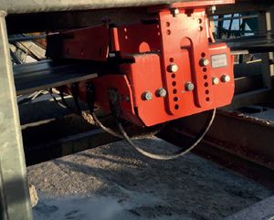 Support orange fixé sous une bande transporteuse avec une sangle courbe, au-dessus de gravier